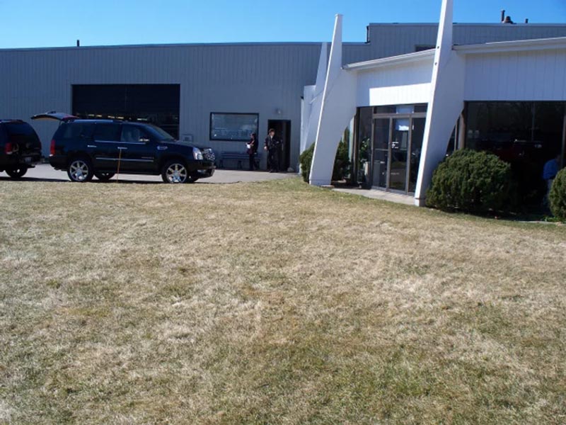 Grass area in front of a building with parked vehicles nearby.