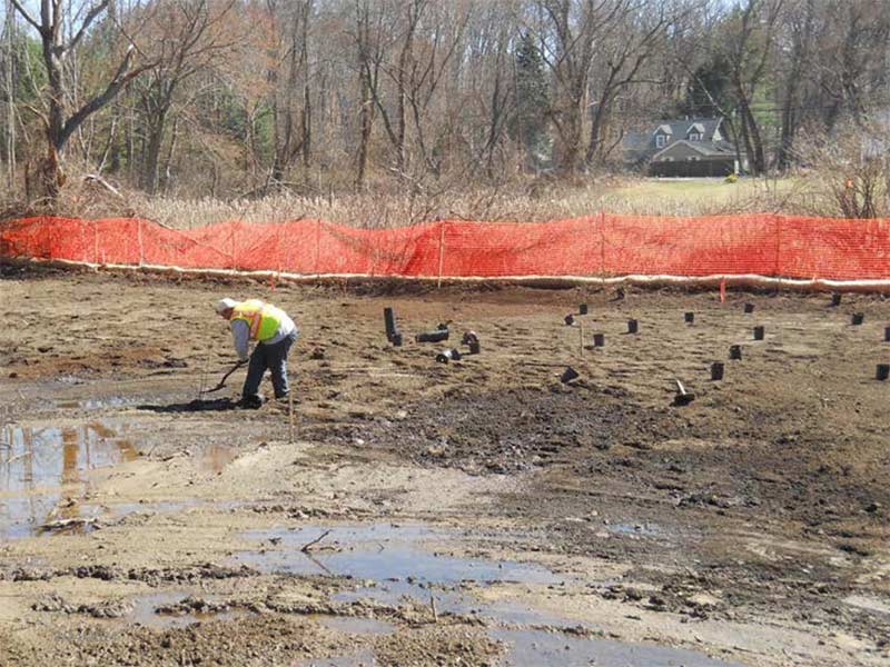 Worker standing in a muddy construction site near an orange safety fence.