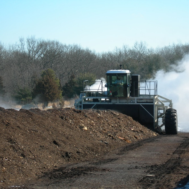 Large industrial machine working on a pile of soil with steam rising in the background.