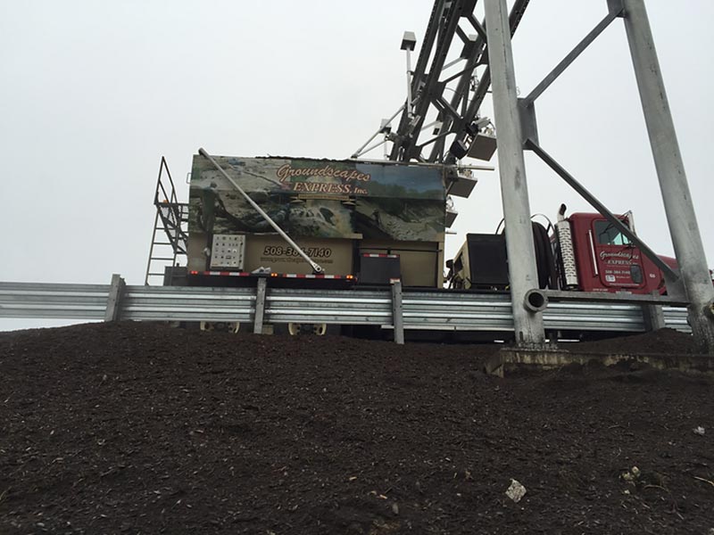 Truck and equipment positioned on a mulched slope beside a metal guardrail.
